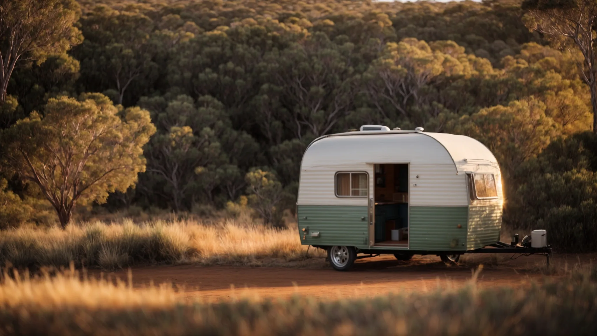 a small family caravan parked amidst serene australian bushland, with the door open invitingly as the sun begins to set.