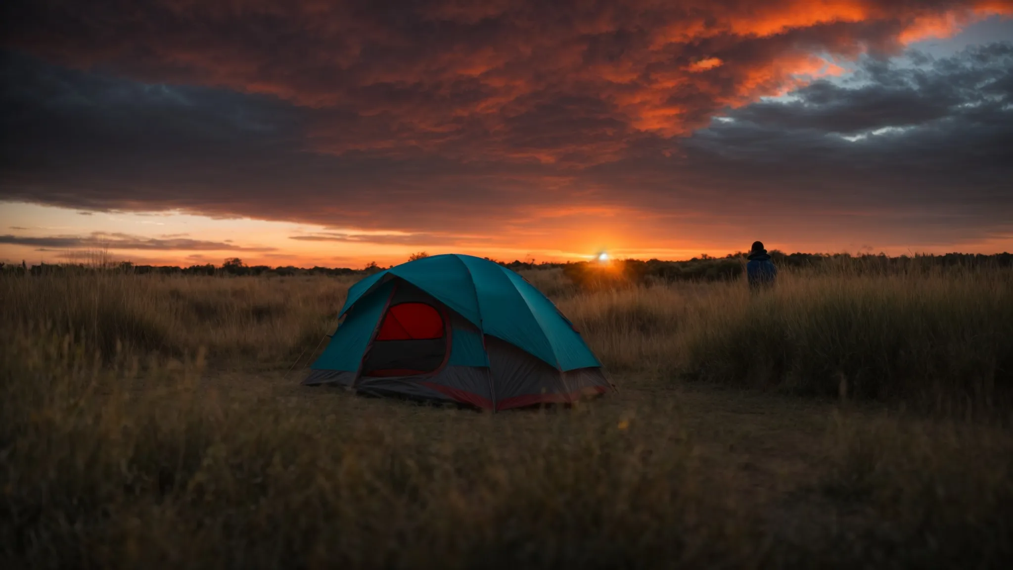 a camper stands in a clearing at sunset, spreading a tent's fabric on the ground against a backdrop of a vibrant sky.