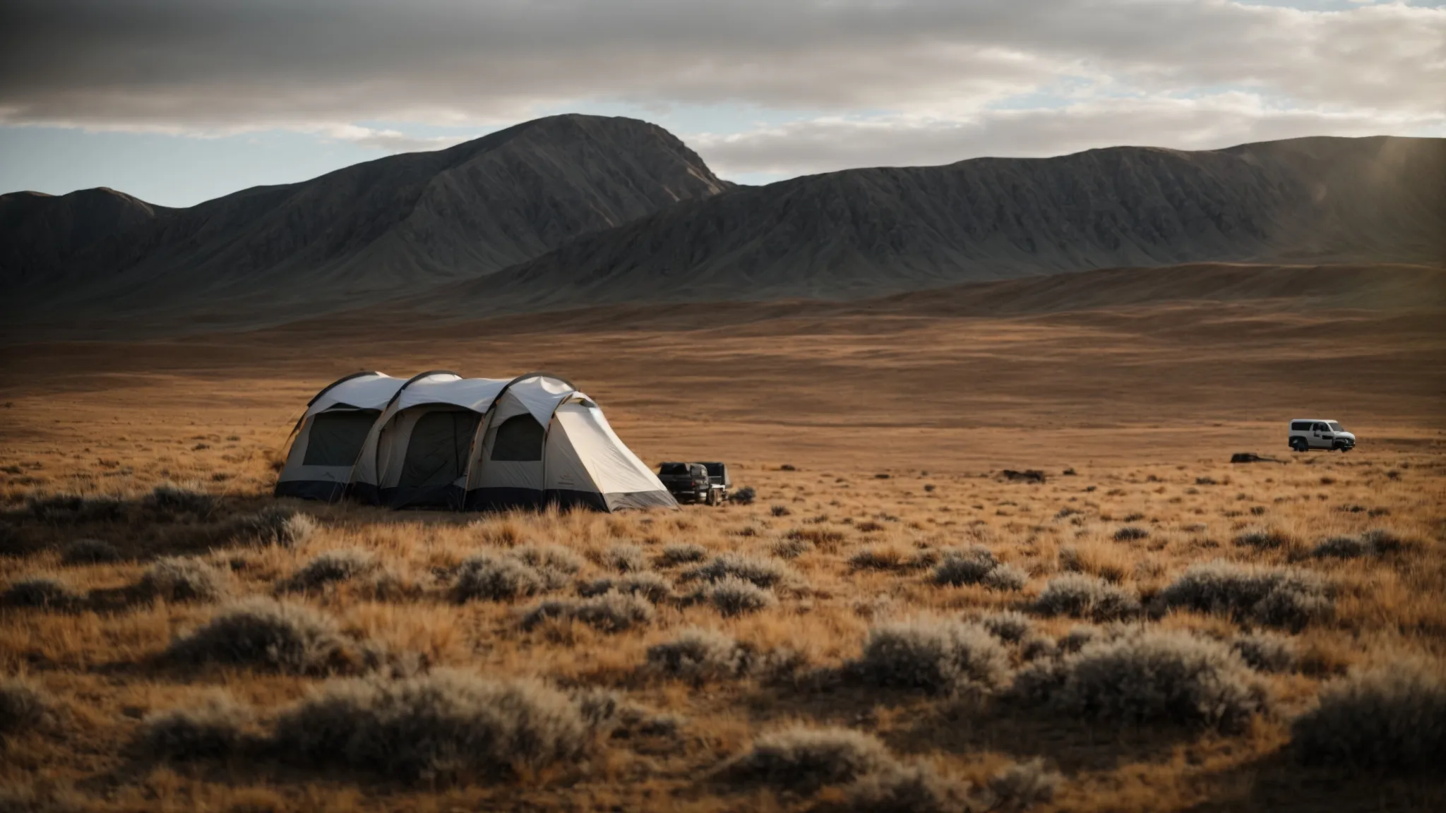 an off-road trailer parked beside a tent in a remote, wild landscape under a vast, open sky.