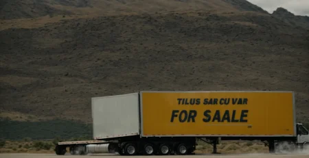 a large semi trailer parked in an open lot with a "for sale" sign prominently displayed.